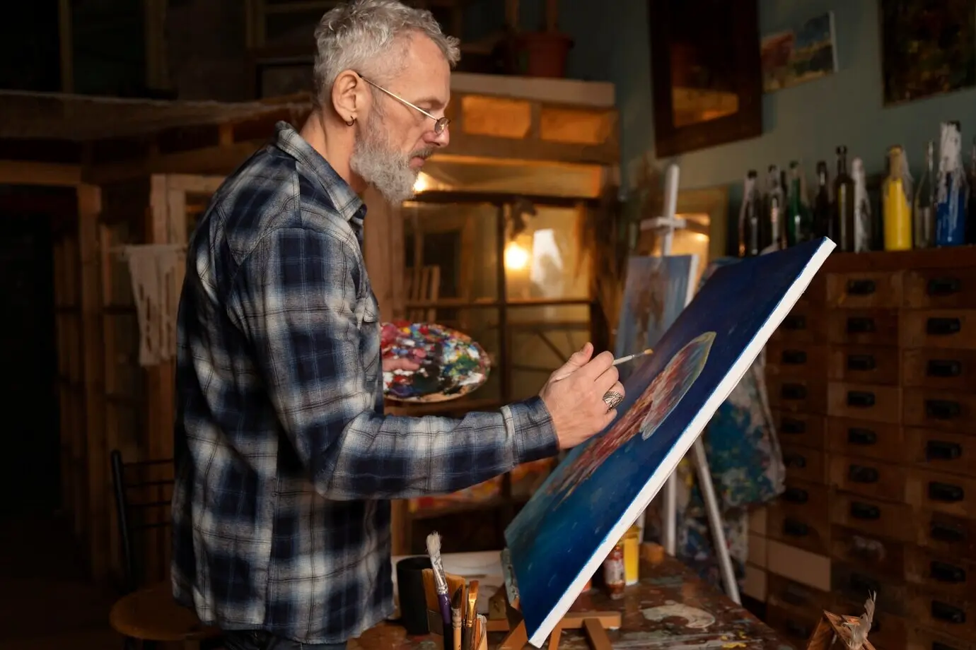 Halbnahe Aufnahme eines älteren Malers in Innenräumen.